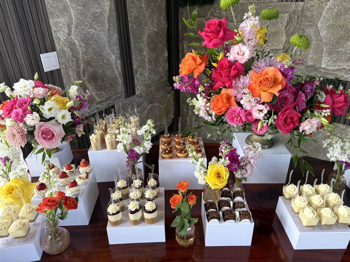 Dessert table with cheesecake shots, mini pavlovas, brigadeiros and bright flower arrangements